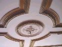 Het gerestaureerde rozet teruggeplaatst in rijk geornamenteerde plafond. Hierna wordt het geheel in de originele kleuren teruggebracht.